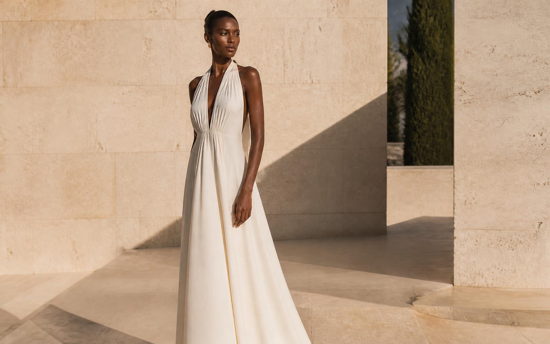 Woman in an ivory Mossane gown in a travertine courtyard at golden hour